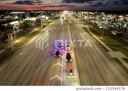 Nighttime traffic stop on USA city street as police pull over speeding vehicle. Patrol car lights flash in urban traffic environment. 131544176
