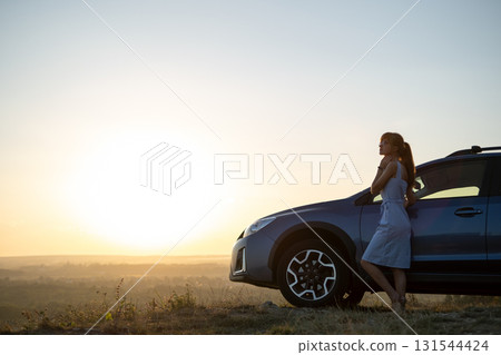 Happy woman driver in blue summer dress enjoying warm evening near her car. Travel and vacations concept. 131544424
