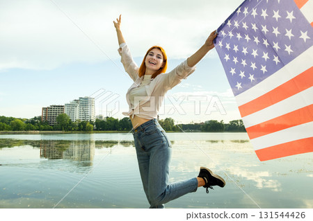 Happy red haired young woman with United States national flag in her hand. Positive girl celebrating US independence day. 131544426