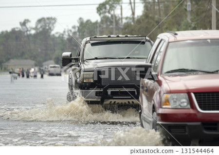 Flooded street after hurricane rainfall with driving cars in Florida residential area. Consequences of natural disaster Flooded street after hurricane rainfall with driving cars in Florida residential area. Consequences of natural disaster 131544464