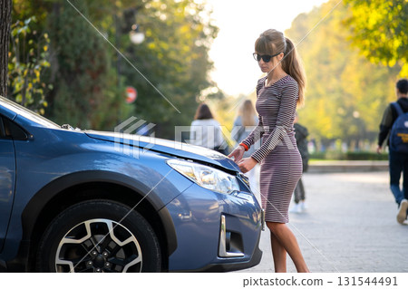 Female driver opening car hood inspecting broken engine on a city street. Female driver opening car hood inspecting broken engine on a city street. 131544491