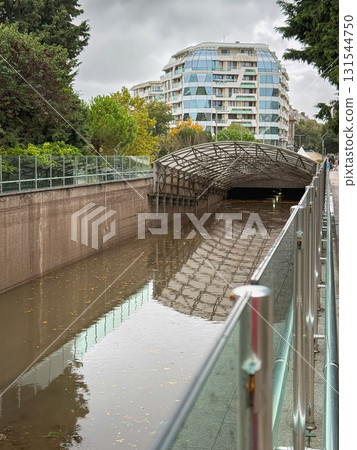 Floodwater fills city Underground Street, underpass beside modern glass buildings after heavy rainfall. Concept of urban flooding, stormwater overflow, and infrastructure challenges 131544750
