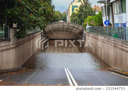 Flooded underpass blocks city road, with fallen leaves and rain-soaked asphalt in the foreground. Concept of flooding, stormwater, and dangerous road conditions 131544753