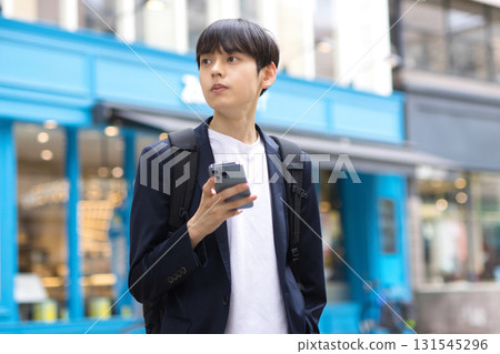 A male businessman in his twenties standing in the street with a smartphone A male businessman in his twenties standing in the street with a smartphone 131545296