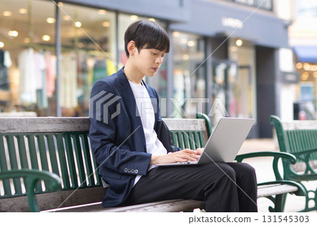 A man in his twenties sitting on a bench and working on a computer A man in his twenties sitting on a bench and working on a computer 131545303