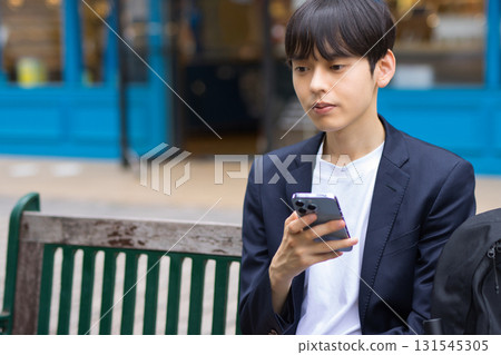 A male businessman in his twenties sitting on a bench and looking at his smartphone 131545305