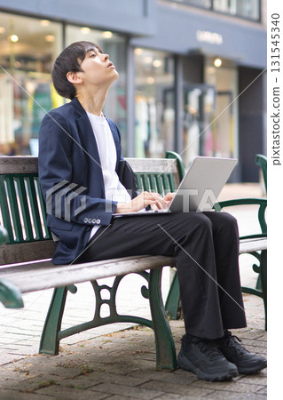 A man in his twenties sitting on a bench and working on a computer 131545340