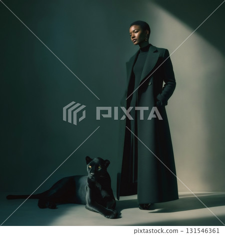 Stylish female model wearing a long dark green coat stands next to a black panther in a professional studio setting, illuminated by dramatic lighting 131546361