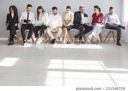 Young office people sits in queue waiting for job interview holding computer devices using internet  131546729