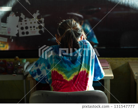 Schoolgirl sitting at desk in colorful tie dye shirt 131547777