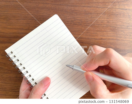 Close-up of a woman's hands writing in a notepad at a wooden desk Close-up of a woman's hands writing in a notepad at a wooden desk 131548069