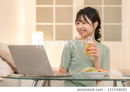 Young Asian woman relaxing and looking at laptop while eating at home in the evening Young Asian woman relaxing and looking at laptop while eating at home in the evening 131548082