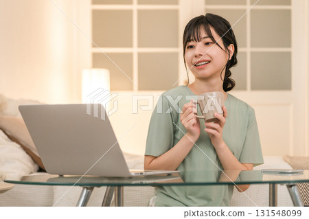 晚上,年輕的亞洲女性在家裡放鬆,看著筆記型電腦,喝著熱飲 晚上,年輕的亞洲女性在家裡放鬆,看著筆記型電腦,喝著熱飲 131548099