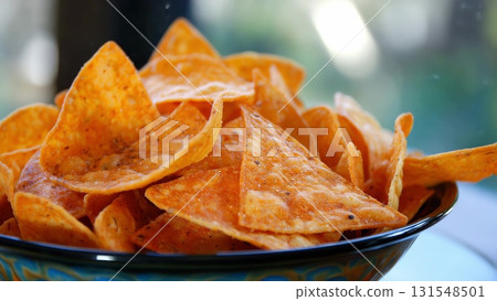 Spicy tortilla chips sitting in ceramic bowl, showcasing golden orange color and crispy texture for snack enthusiasts 131548501