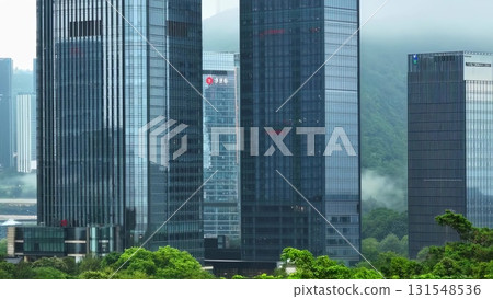 Urban skyline rising behind swaying green trees, merging natural landscape with contemporary architectural silhouettes, representing city environmental balance 131548536