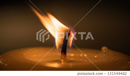 Close up of a single candle flame burning with a warm glow in a dark, peaceful setting 131549482