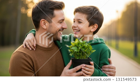 Happy father and son embracing, holding a green potted plant outdoors at sunset Happy father and son embracing, holding a green potted plant outdoors at sunset 131549573