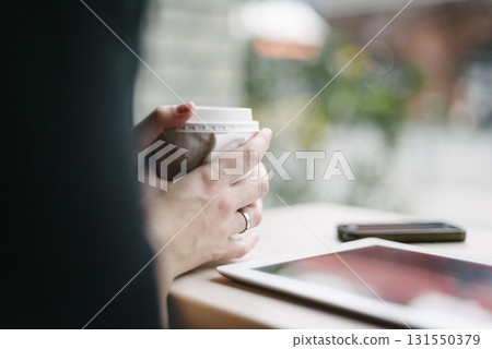 Hands holding coffee cup near tablet and phone 131550379
