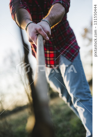 Man chopping wood with axe in rural field 131550444