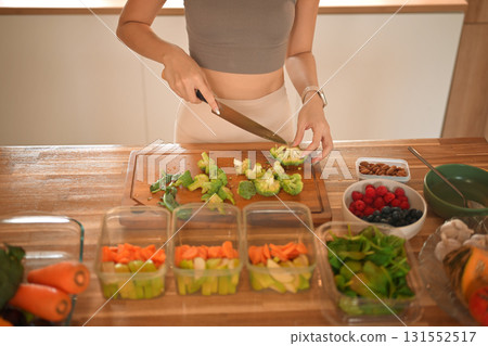 Closeup woman chopping broccoli and dividing food into meals weekend meal prep for weight loss Closeup woman chopping broccoli and dividing food into meals weekend meal prep for weight loss 131552517