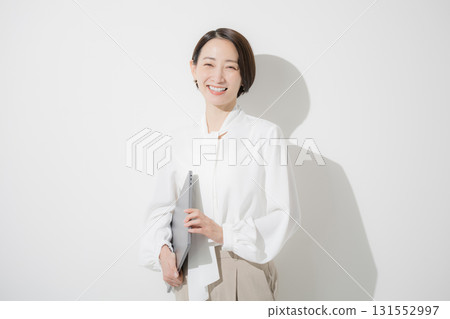 A beautiful woman in office casual wear and a blouse standing with a laptop on a white background, looking at the camera A beautiful woman in office casual wear and a blouse standing with a laptop on a white background, looking at the camera 131552997