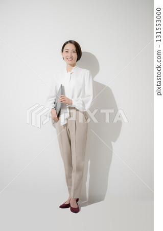 A beautiful woman in office casual wear and a blouse standing with a laptop on a white background, looking at the camera 131553000