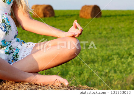Pregnant yoga woman sitting on a haystack in the green grass field Pregnant yoga woman sitting on a haystack in the green grass field 131553053
