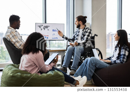Young professionals discussing global business report on monitor in relaxed office environment. Group includes diverse race, genders, ages, featuring inclusivity and teamwork. Young professionals discussing global business report on monitor in relaxed office environment. Group includes diverse race, genders, ages, featuring inclusivity and teamwork. 131553438