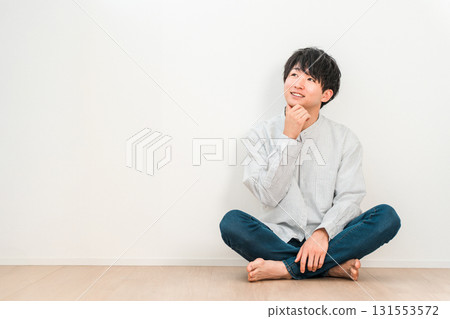 A young Asian man sitting cross-legged in a living room with white walls (Imagination, Dream, Thinking, Conception, Plan) A young Asian man sitting cross-legged in a living room with white walls (Imagination, Dream, Thinking, Conception, Plan) 131553572