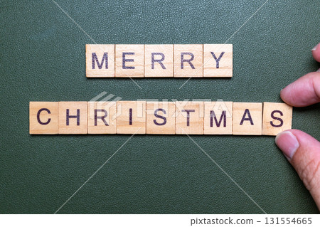 Hands arranging wooden letter blocks spelling Merry Christmas on green background Hands arranging wooden letter blocks spelling Merry Christmas on green background 131554665