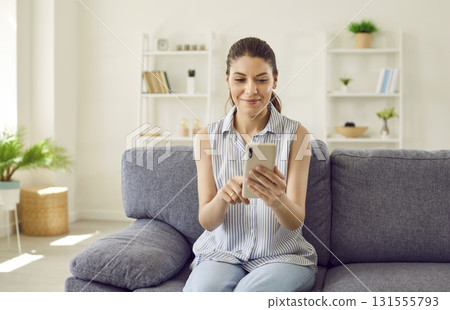 Young woman sitting on couch at home and browsing social media on her cell phone Young woman sitting on couch at home and browsing social media on her cell phone 131555793