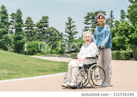 坐在輪椅上的祖母和她的孫女在公園散步 坐在輪椅上的祖母和她的孫女在公園散步 131556190