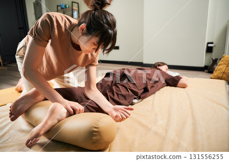 Masseuse making thai yoga massage. Woman therapist doing traditional massage treatment for female patient using elbow. Client lying on mat, meditating, enjoying hand massage in calm atmosphere. 131556255