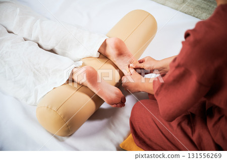 Masseuse making thai yoga massage. Woman therapist doing traditional massage treatment for female patient. Client lying on mat, meditating, enjoying hand massage in calm atmosphere. Cropped view. 131556269