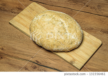 First-person view of round loaf of homemade rye bread placed on a wooden bamboo cutting board on a hardwood texture countertop. Baking concept, symbol of happy family life 131556461