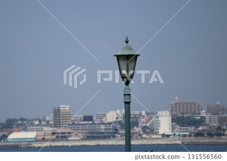 A landscape photographed with a stylish street lamp in focus against a backdrop of blue sky, sea, and cityscape. A landscape photographed with a stylish street lamp in focus against a backdrop of blue sky, sea, and cityscape. 131556560
