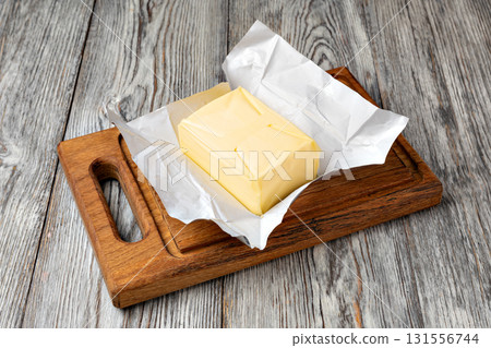 Stick of butter wrapped in foil on wooden cutting board Stick of butter wrapped in foil on wooden cutting board 131556744