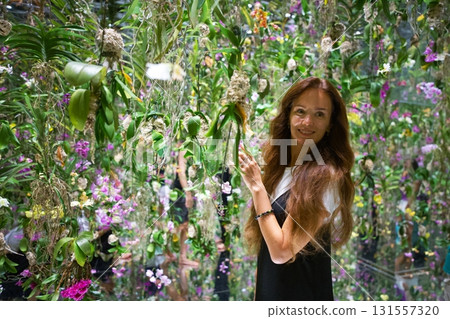 Smiling woman surrounded by vibrant orchids and greenery 131557320