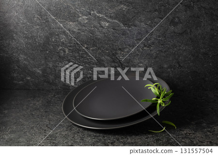 Empty round black plates with rosemary on a black stone background. Empty round black plates with rosemary on a black stone background. 131557504