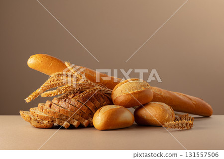 Sliced bread, baguette, and French buns with wheat ears on a beige background. 131557506
