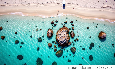 An expansive beach scene with turquoise waters, a rocky shoreline, and multiple people enjoying the sunny day. 131557507