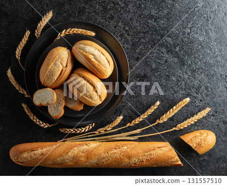 Baguette, French buns, and wheat ears on a black stone table. 131557510