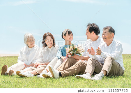 A park with a view of the blue sky, a family sitting on a hill, parents and children, a three-generation family (father, mother, daughter, grandmother, grandfather) 131557735