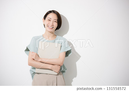 一位身著辦公室休閒服的漂亮女士站著，拿著筆記型電腦，看著相機，上身，白色背景，微笑著的商業形象 131558572