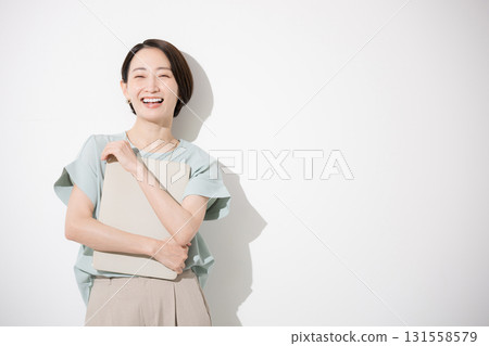 Business image of a beautiful woman in office casual wear standing with a laptop, looking at the camera, upper body, white background, smiling 131558579