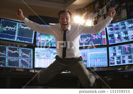 Trader jumping in joy at trading desk with glowing charts 131559553