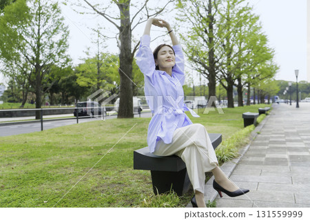 Portrait of a young businesswoman sitting and stretching in a park in an office district Portrait of a young businesswoman sitting and stretching in a park in an office district 131559999
