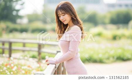 A woman leaning against a railing in a park with a calm expression 131562185