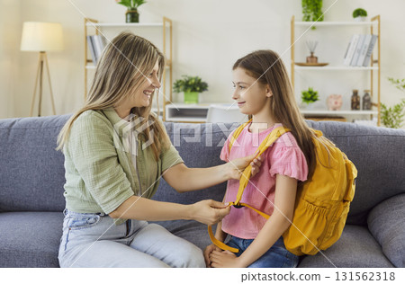 Mother helping daughter with yellow backpack at home before school morning 131562318