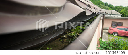 Dirty gutter under the roof clogged with moss and debris Dirty gutter under the roof clogged with moss and debris 131562409